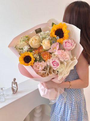 A woman in a blue dress proudly holds a sunflower bouquet on her university graduation day in Kuala Lumpur.