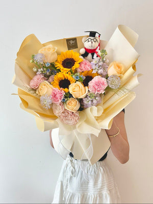 A woman celebrates her university graduation in Kuala Lumpur, holding a large size sunflower bouquet and a stuffed bear.