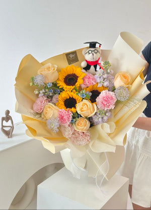 A woman in Kuala Lumpur holds a large sunflower bouquet and a stuffed bear, celebrating her university graduation day.