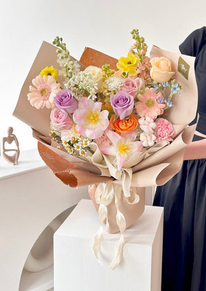 A woman in a black dress holds a birthday bouquet of tulips and mixed roses, set in a studio.
