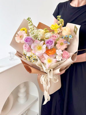 A woman wearing a black dress holds a vibrant birthday bouquet of tulips and mixed roses, in a studio setting.