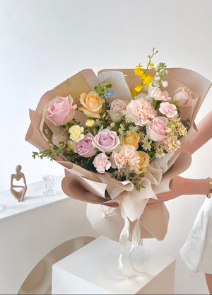 A woman stands in her office studio, holding a bouquet of mixed roses wrapped in khaki, radiating joy and warmth.