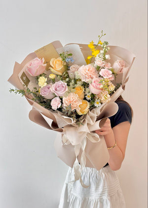 A woman in an office studio holds a mixed rose bouquet wrapped in khaki paper, smiling gently at the camera.