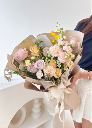 In her office studio, a woman holds a khaki-wrapped bouquet of mixed roses, showcasing a cheerful expression.