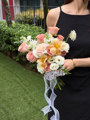Bouquet of cappuccino ROM flowers held by a person wearing a black sleeveless top, with a blurred outdoor background.
