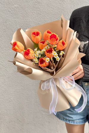A woman in a black cardigan holds a bouquet of orange tulips in Kuala Lumpur for her friend's birthday celebration.