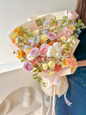 Elegant bouquet showcasing a mix of purple, peach, and ivory flowers, accented with greens and whimsical fillers.