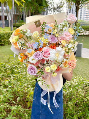 Bouquet of colorful flowers held by a person outdoors with greenery in the background