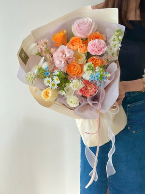 A pastel and bright-hued bouquet perfect for celebrations, held up against a neutral wall.