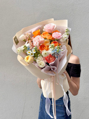 A lush floral arrangement wrapped in cream and mauve paper, showcasing a colorful mix of seasonal blooms.