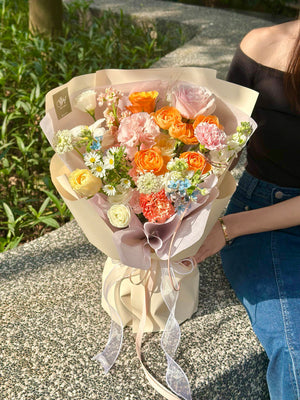 A hand-tied bouquet with a cheerful blend of roses, carnations, daisies, and delicate blue accents held by a woman in denim.