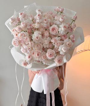 Bouquet of pink kiss of fairy rose spray held by a person against a neutral background with warm lighting behind.