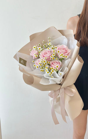 A woman wearing a black dress holds a bouquet of pink roses and chamomile at a restaurant for her girlfriend's birthday.