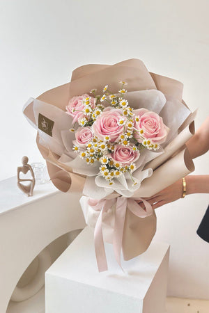 A girl in a black dress offers a bouquet of pink roses and chamomile for her girlfriend's birthday party at a restaurant.