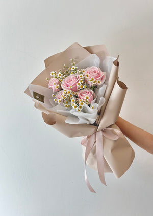 A woman hand is holding a birthday bouquet of pink roses and chamomile for her girlfriend at a restaurant.