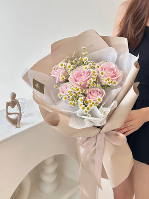 A woman in a black dress holds a bouquet of pink roses and chamomile for her girlfriend's birthday at a restaurant.
