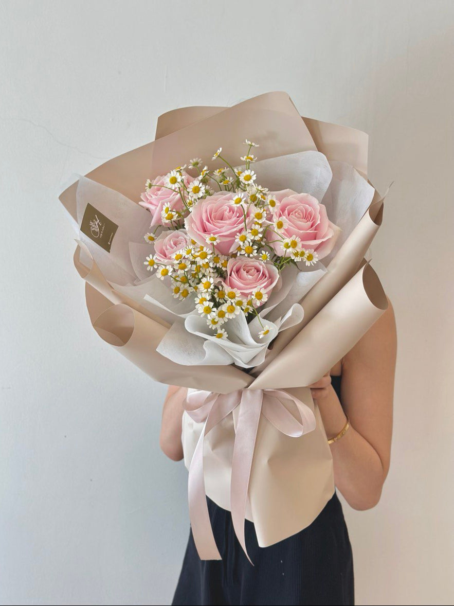 A girl in a black dress presents a mixed bouquet of pink roses and chamomile for her girlfriend's birthday celebration.