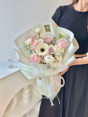 A girl wearing a black dress smiles while holding a bouquet of flowers in front of a camera.