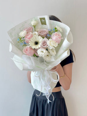 A woman in a black dress holds a bouquet of flowers, posing in front of a camera.