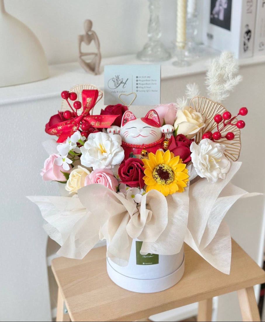 A round white box adorned with a bouquet of flowers, featuring a lucky cat on top for a business opening in Kuala Lumpur.