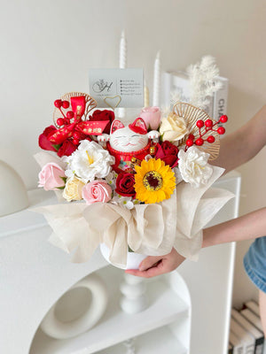 A girl is handing a white box with a floral bouquet and a lucky cat on top, marking a business opening event in Kuala Lumpur.