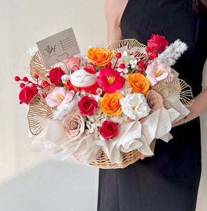 Basket arrangement with red, orange, and blush roses, featuring a lucky cat for opening ceremony wishes.