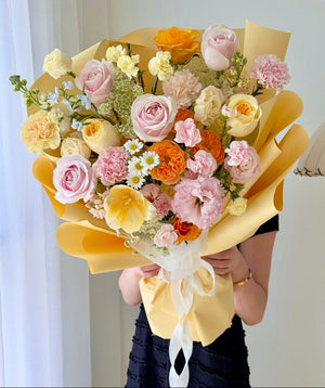 Cheerful pastel mixed rose bouquet with yellow wrapper featuring pink roses and orange flowers, perfect for birthday surprises and happy occasions.