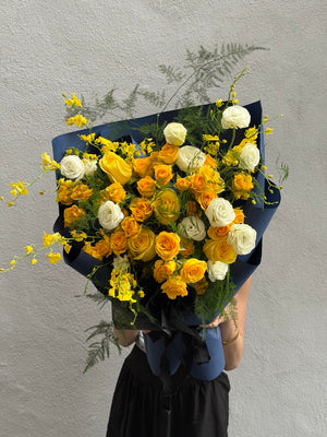 Bouquet of yellow, white, and orange roses with asparagus grass against a gray background at Kuala Lumpur.