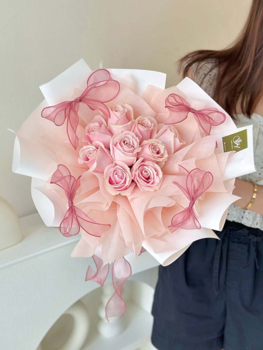 9 pink rose wrapped with white wrapper is holding by a girl.