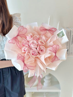 A girl is holding a 9 pink roses with 4 pink ribbon around the wrapper.