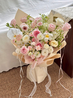 Elegant floral arrangement with blush roses, chamomile, and delicate white tulip wrapped in cream and pink paper.