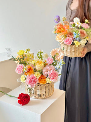 A woman wearing a brown top holds a flower basket, while another basket rests on a table, suitable for any occasion.