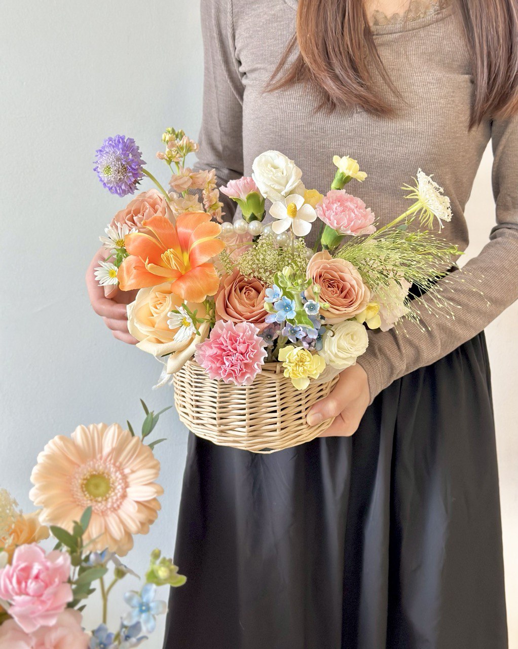 A woman wearing a brown top holds a flower basket, while another basket rests on a table, suitable for any occasion.