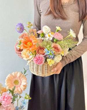 A woman wearing a brown top holds a flower basket, while another basket rests on a table, suitable for any occasion.