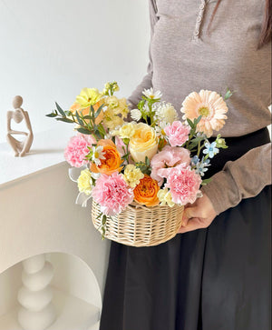 A woman wearing a brown top holds a flower basket, suitable for any occasion.