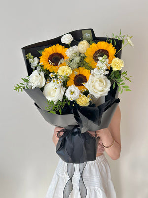 Elegant black-wrapped graduation bouquet with sunflowers, white blooms, and fresh greenery.