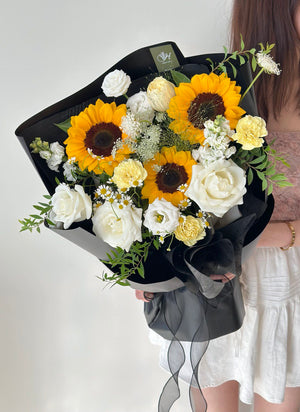 Bouquet of sunflowers and white flowers held by a person against a plain background.