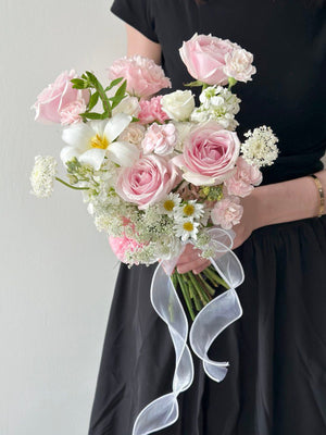 Woman in black dress holding a pastel pink and white bridal bouquet tied with a flowing white ribbon.