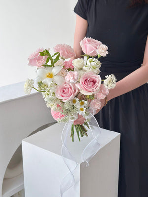 Feminine and graceful bouquet with roses, carnations, and white tulip, accented with greenery and a white ribbon, perfect for bridal bouquet.