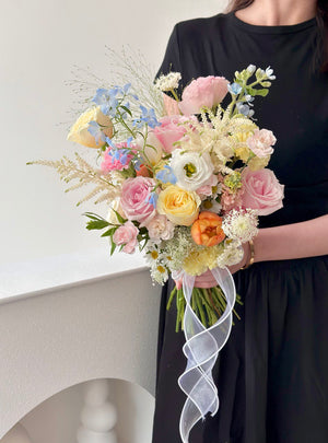 Bouquet of pastel flowers held by a person wearing a black dress against a white background