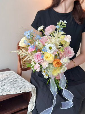 Vibrant wedding bouquet mixing soft pastel shades with pops of bright yellow and orange holding by a person sitting on a chair.