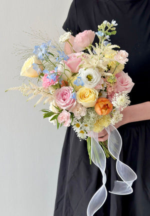 Bouquet of bridal pastel flowers held by a person wearing a black dress against a gray background