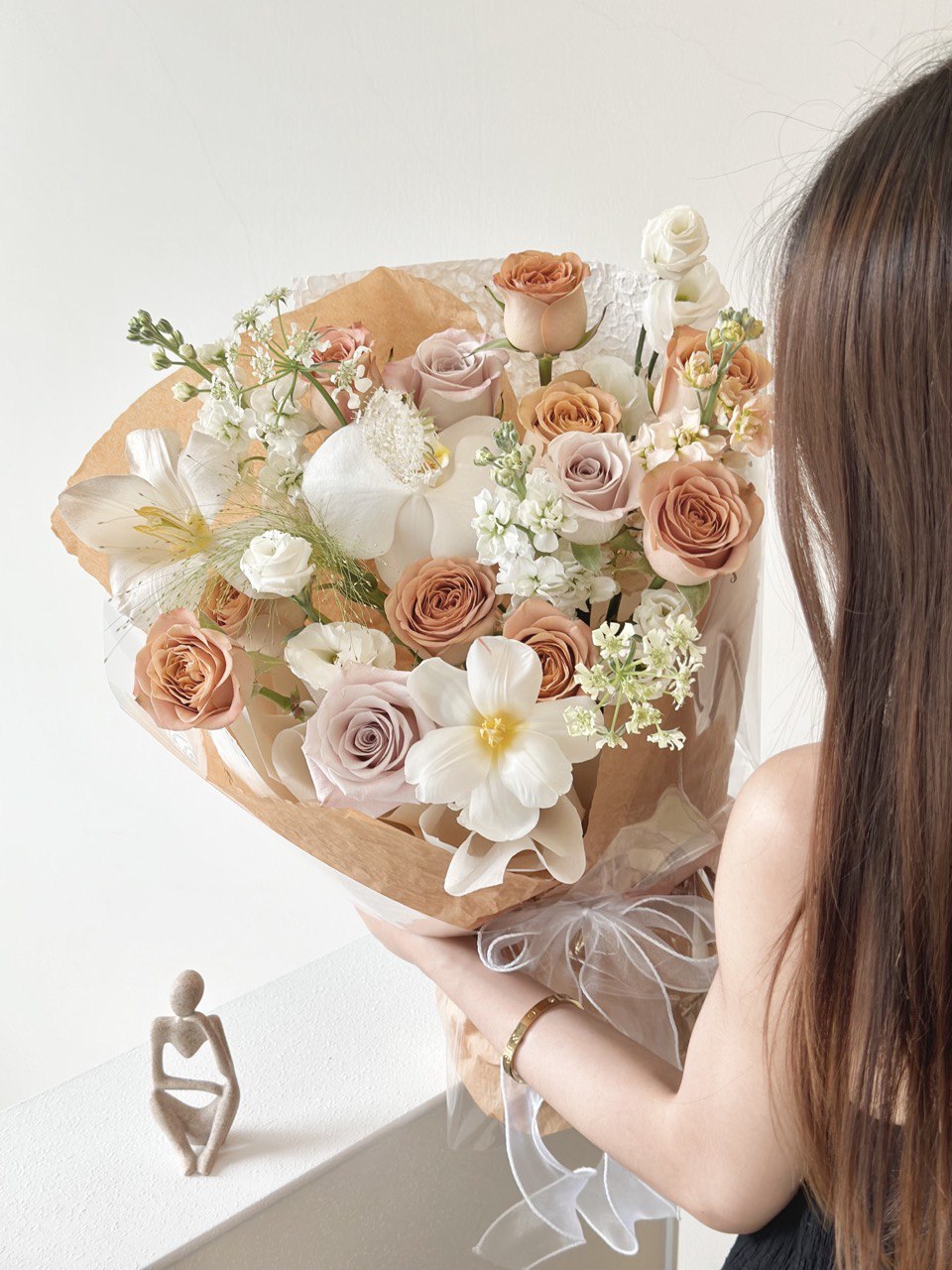 A woman wearing a black dress holds a bouquet of cappuccino roses, celebrating her birthday in Kuala Lumpur.