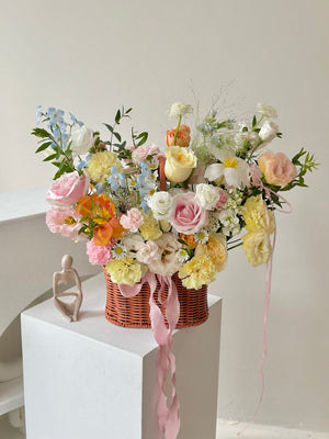 Bouquet of flowers in a basket with a small sculpture on a white pedestal against a light background, perfect for speedy recovery gift.