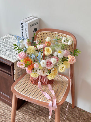 Floral arrangement in a basket on a wicker chair with a Chanel book in the background.