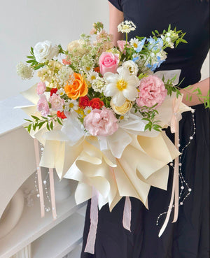 Close-up of a pastel floral arrangement with roses, carnations, and tulip, wrapped in layered cream wrapping paper.