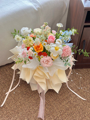 Elegant mixed flower bouquet featuring orange, pink, white, and blue blooms with cascading ribbons and pearl accents.