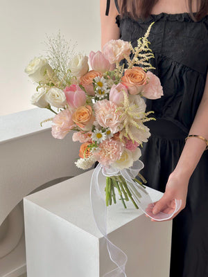 Delicate hand-tied wedding bouquet with mixed blooms in blush, white, and cappuccino, finished with a flowing white ribbon.