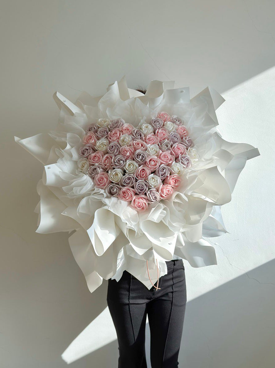 52 rose soap flower heart-shaped arrangement of pink, white and yam soap rose flowers with white ballet wrapper on a plain background - ideal for proposal.