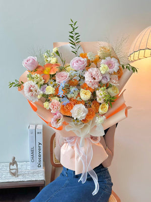 Person holding a colorful bouquet of flowers with a light blue wall and books in the background.